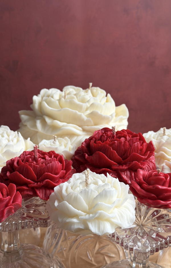 Lumânări decorative în formă de bujor, albe și roșii, sculptate manual, așezate pe suporturi din sticlă, cu detalii fine și aspect elegant.